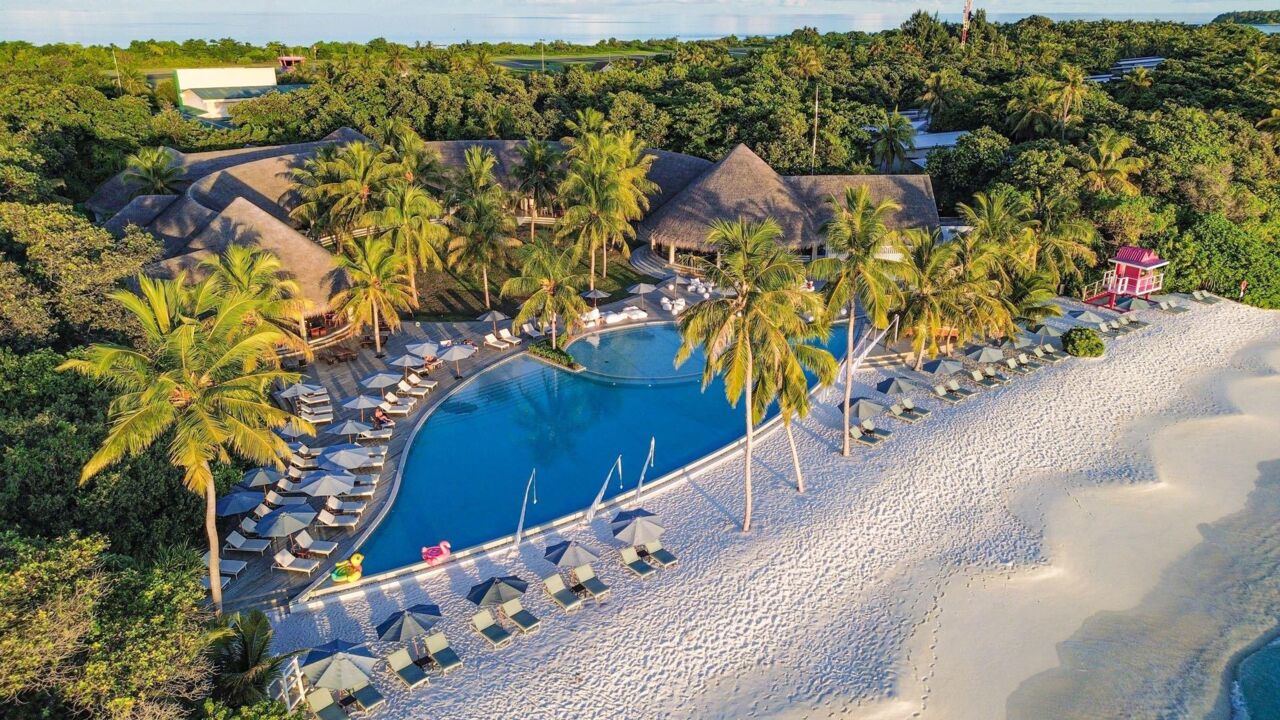 Luftaufnahme eines tropischen Resorts mit großem Pool, Palmen, Liegestühlen auf Sandstrand und angrenzendem Meer.