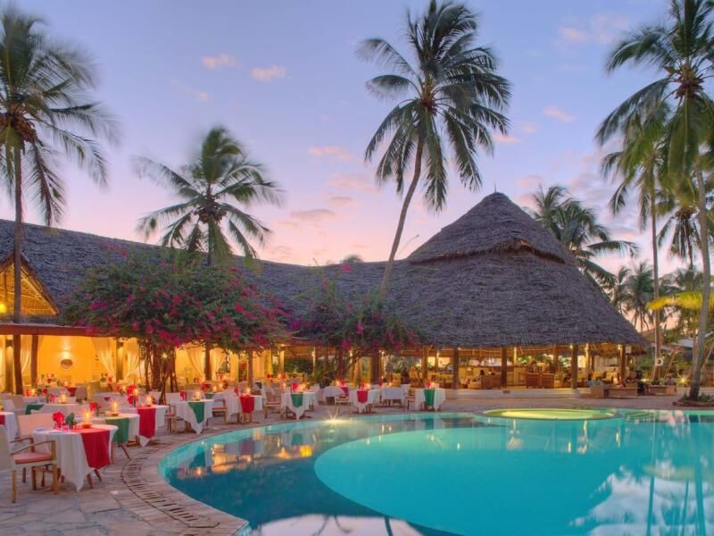 Beleuchtetes Restaurant mit gedeckten Tischen und Strohdach neben einem Pool