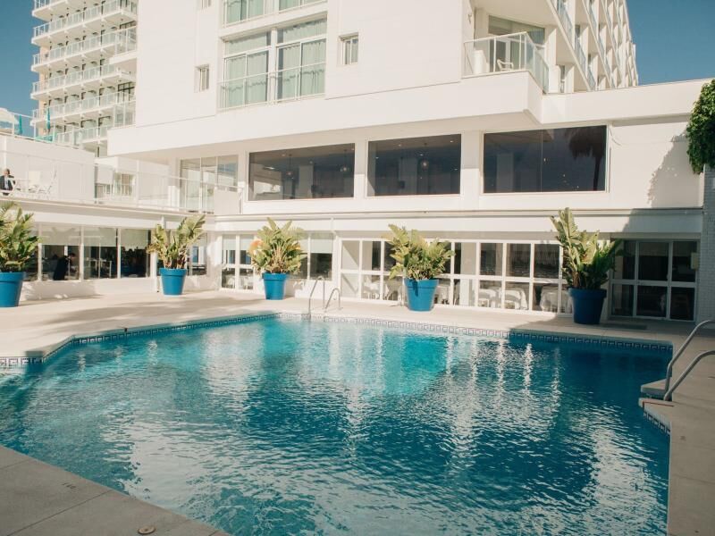 Großer rechteckiger Außenpool vor einem mehrstöckigen weißen Hotelgebäude