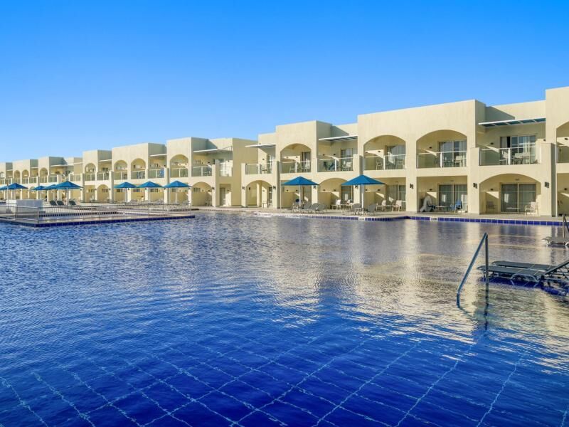 Großer blauer Pool vor einer langen, zweistöckigen Hotelanlage