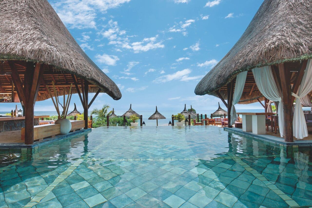 Infinity-Pool mit türkisfarbenen Fliesen zwischen zwei strohgedeckten Pavillons