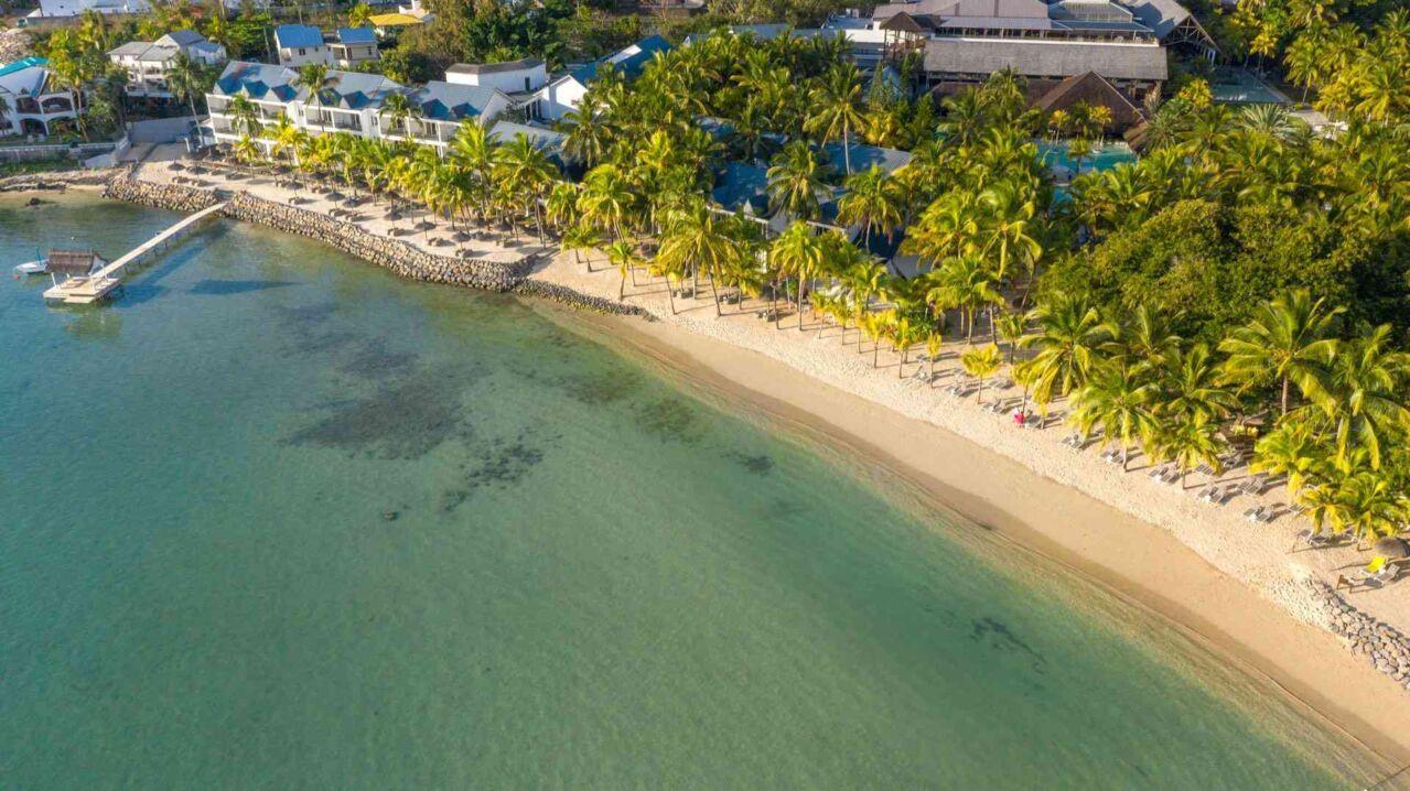 Strand mit klarem Wasser, Palmen und Gebäuden