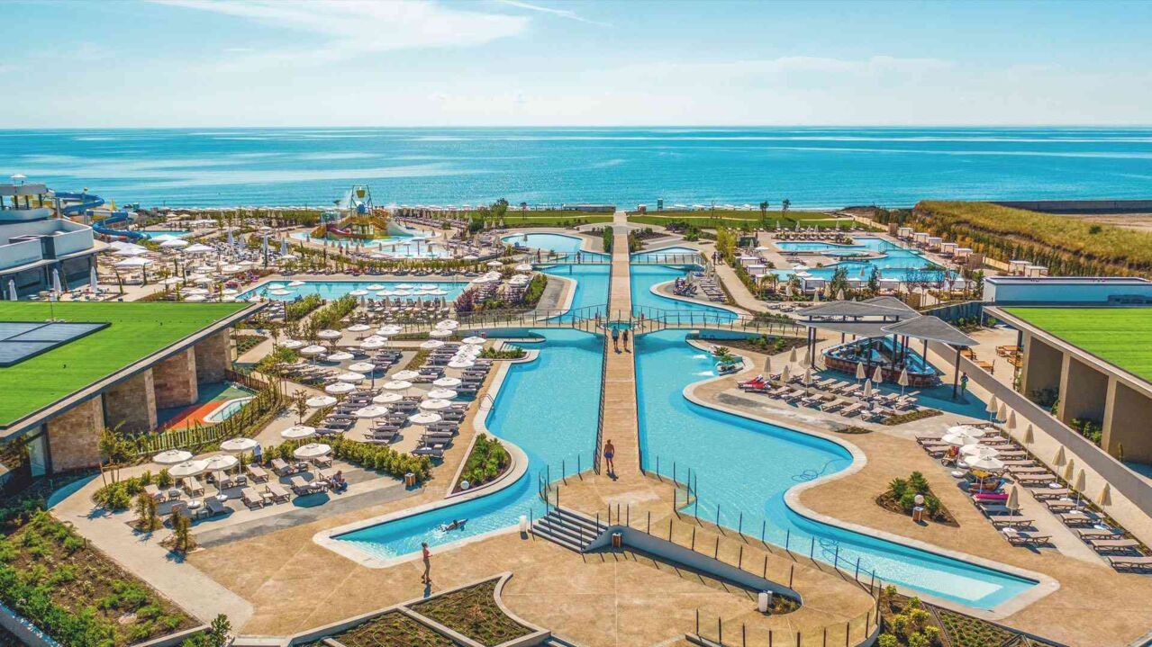 Große Poolanlage mit mehreren Schwimmbecken, Liegestühlen und Sonnenschirmen an der Küste mit Blick auf das Meer