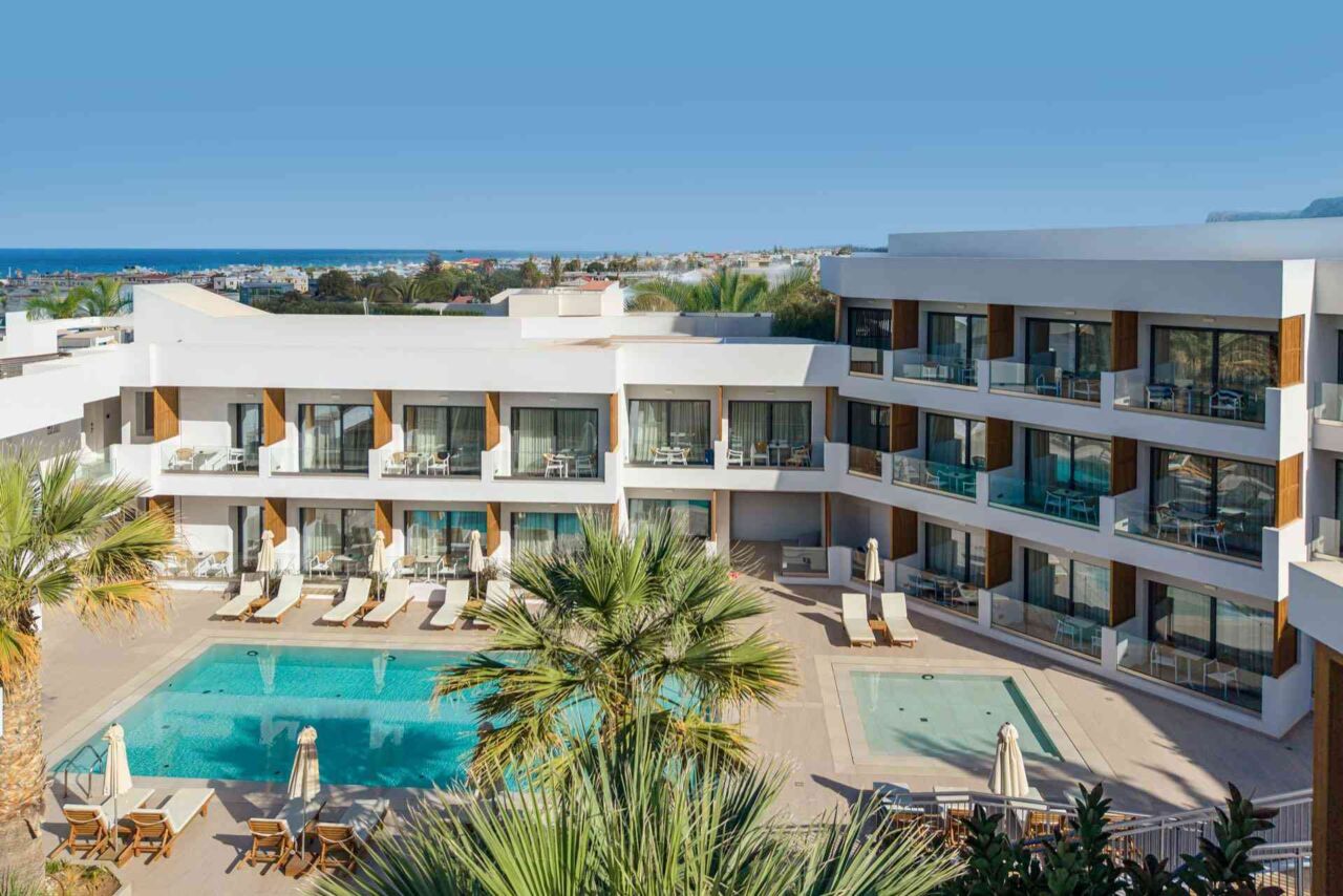 Hotelgebäude mit mehreren Etagen und Balkonen um einen Innenhof mit zwei Schwimmbecken und Liegestühlen