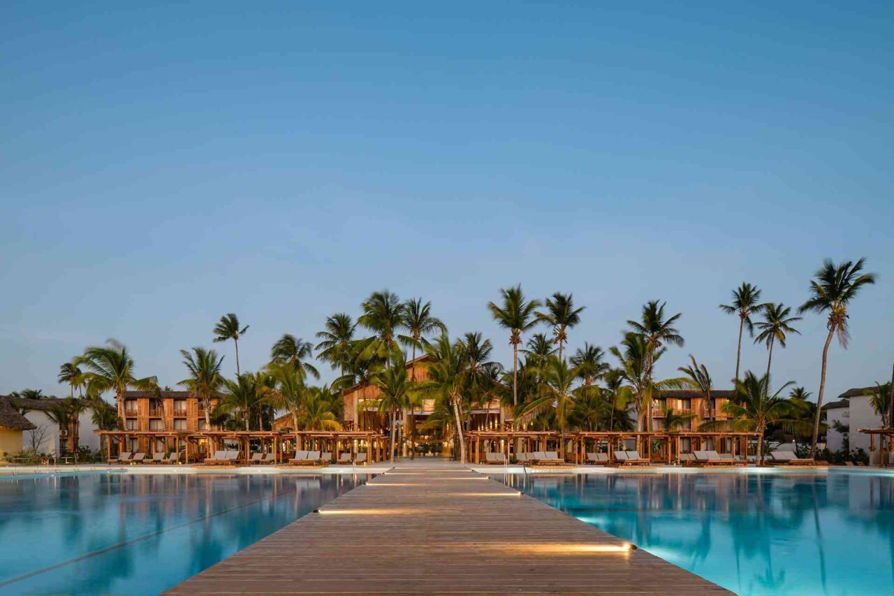 Holzsteg führt zu einem Hotelgebäude mit Palmen