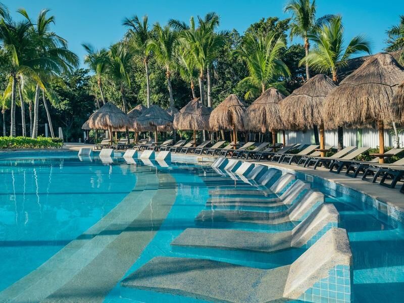 Pool mit Liegestühlen im Wasser und Palmen