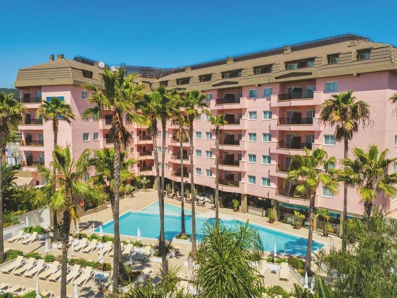 Mehrstöckiges rosa Hotelgebäude mit Pool und Palmen davor