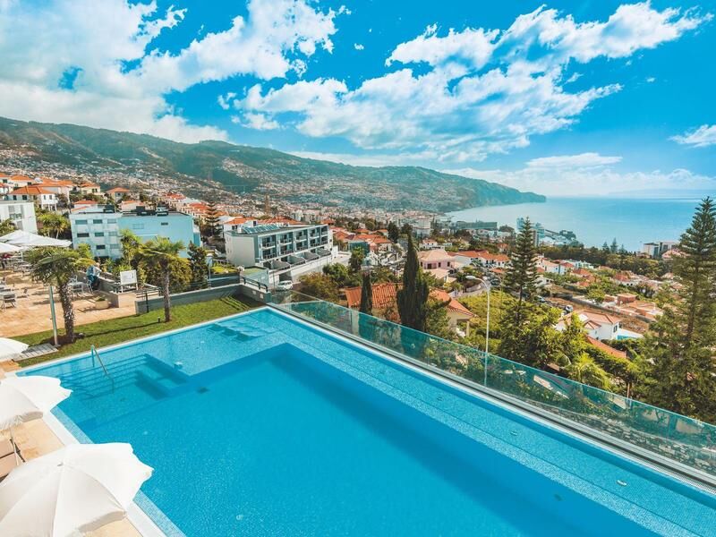 Infinity-Pool mit Glasgeländer vor einer Küstenstadt