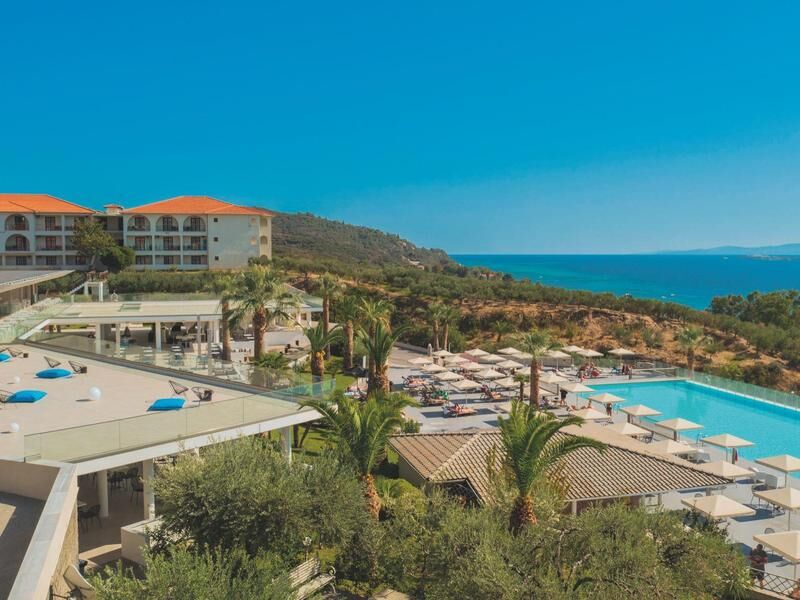 Hotelanlage mit Pool, Liegen und Sonnenschirmen vor hügeliger Küstenlandschaft