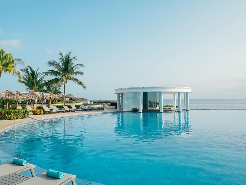 Großer Pool mit Liegestühlen und Palmen am Rand sowie rundem, weißem Pavillon