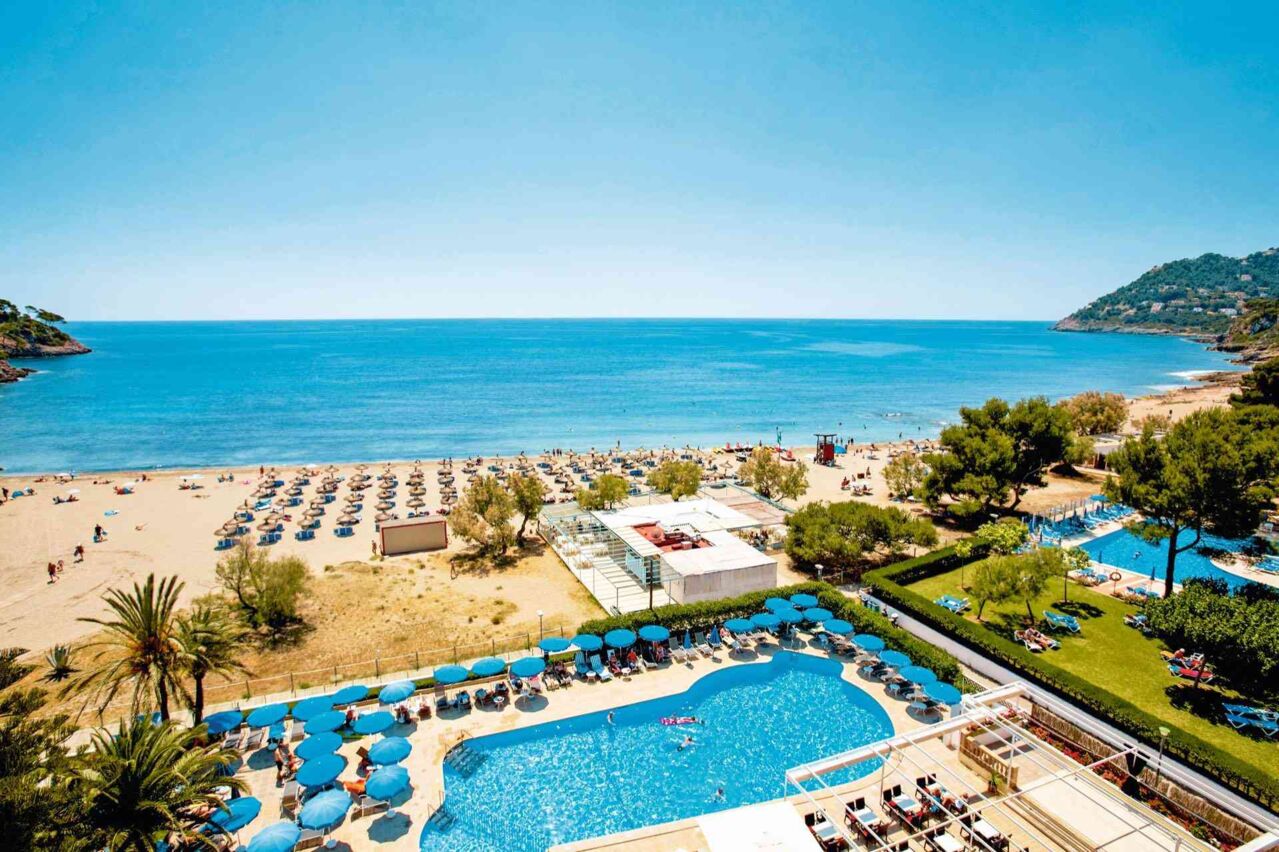 Blick auf einen Hotelpool mit Liegen und Sonnenschirmen am Strand
