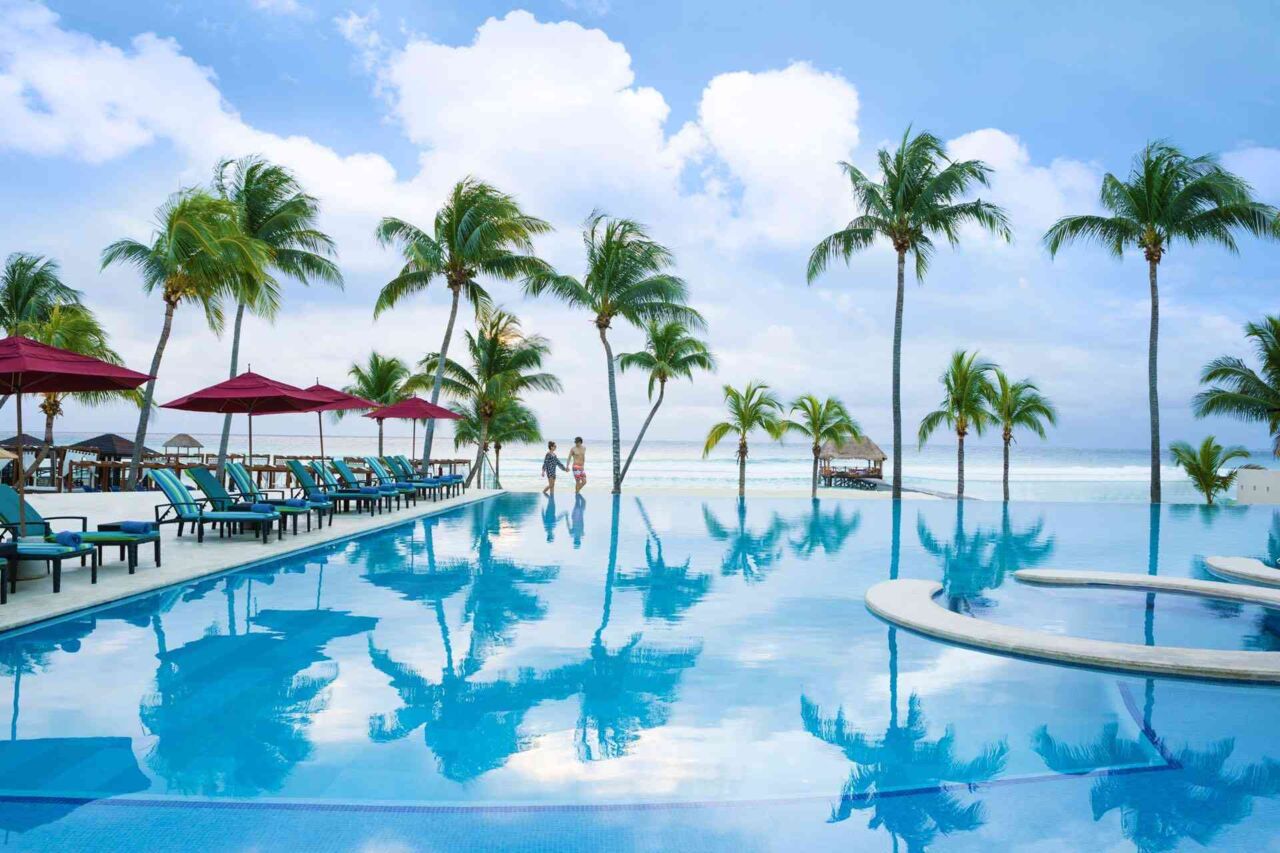Großer Pool mit Liegestühlen und Sonnenschirmen neben Palmen
