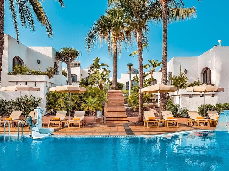 Pool vor weißer Hotelanlage mit Palmen
