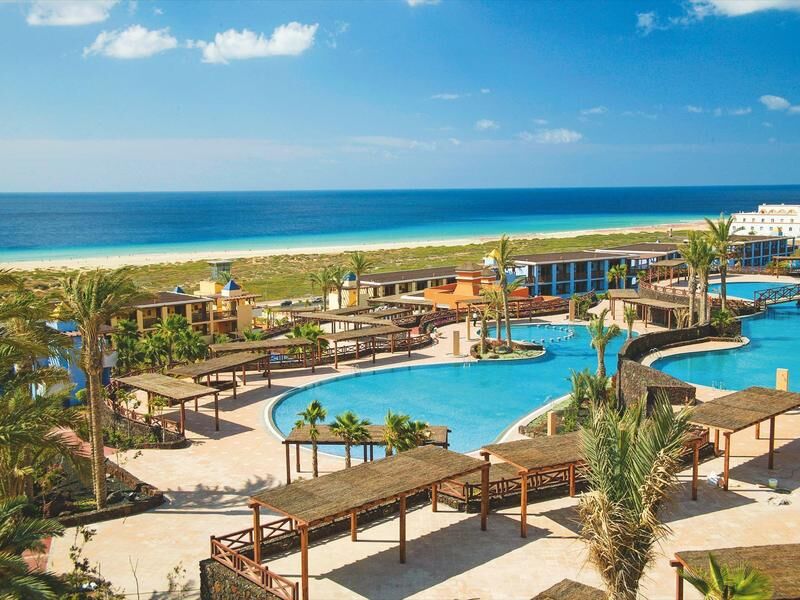 Blick auf eine Hotelanlage mit einem großen Pool und Palmen am Meer