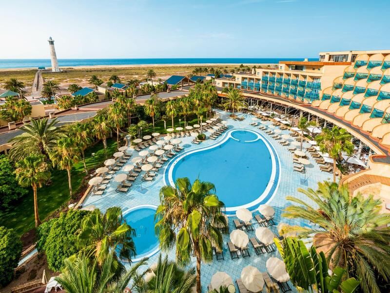 Hotelanlage mit großem Pool, umgeben von Liegestühlen und Palmen