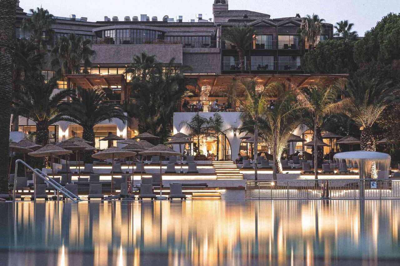 Luxuriöses Hotelgebäude mit beleuchtetem Pool und Palmen