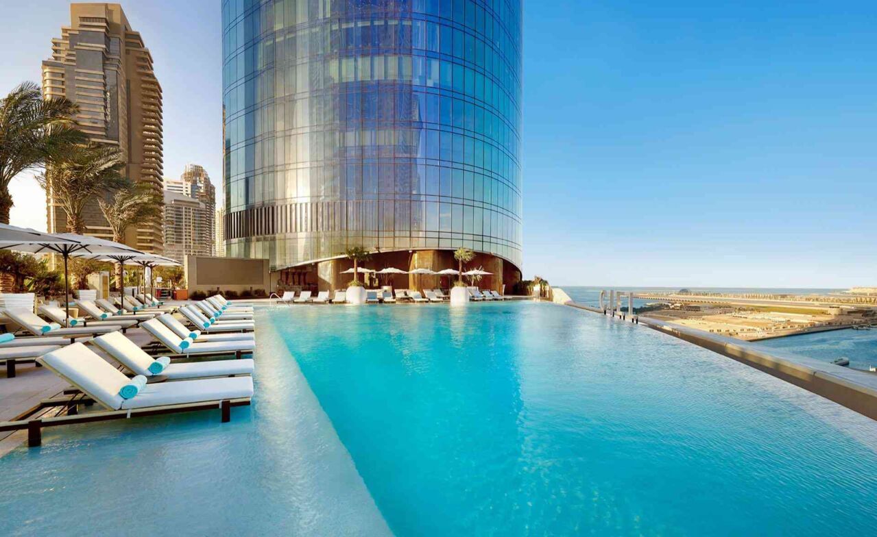 Infinity-Pool mit Liegen vor einem hohen Glasgebäude
