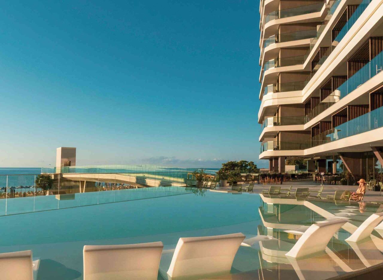 Moderner Hotelkomplex mit mehreren Balkonen und Infinity-Pool mit Liegestühlen am Meer