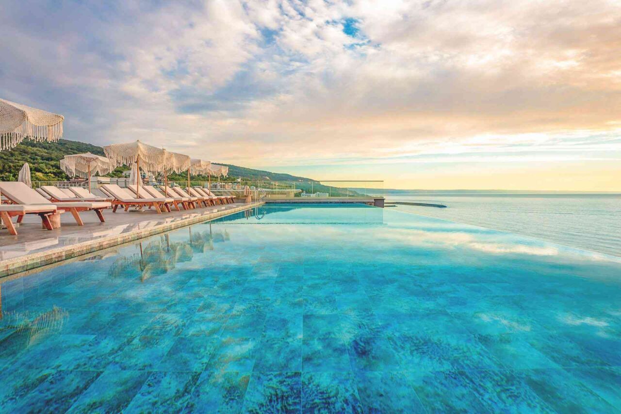 Großer Infinity-Pool mit Liegestühlen und Sonnenschirmen am Rand unter bewölktem Himmel